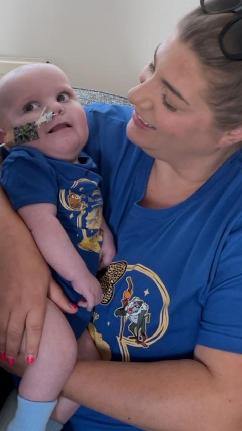 Mum holding baby who is looking off camera with a medical tube from his nose. Mum is smiling at him. They are both wearing blue.