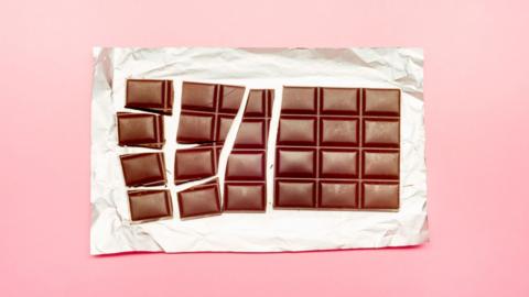 A bar of chocolate broken up into pieces on a foil wrapper.