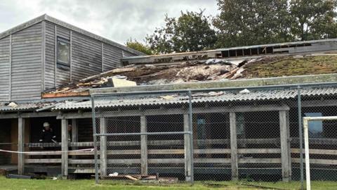 A wooden building in a field with significant fire damage to its roof.