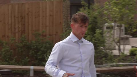 Kian Monks, who has short dark hair and is wearing a white shirt, is walking towards the court building. 