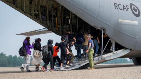 Canadian Armed Forces official assists residents onto a transport aircraft during a wildfire evacuation