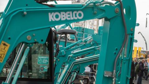 A set of green Kobelco diggers arranged in a line, with the logo displayed on the arms.