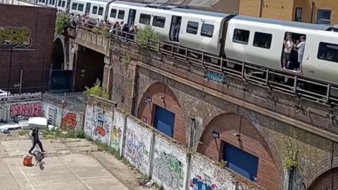 A man with a bike stands below a rail bridge where a train is parked.