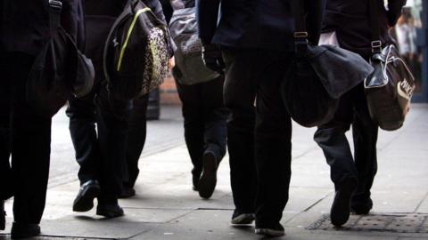 A generic image showing a handful of students, carrying bags, walking away from the camera.