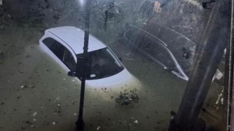 A white car is surrounded by water. The photo was taken at night from above. 