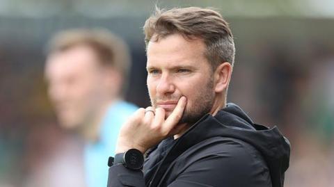Plymouth boss Tom Cleverley looking thoughtful with left handresting on his left cheek, wearing black waterproof jacket