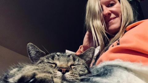 The cat, Elodie, and owner Rachel Rogers. The cat is a tabby and Rachel is wearing an orange jumper. 