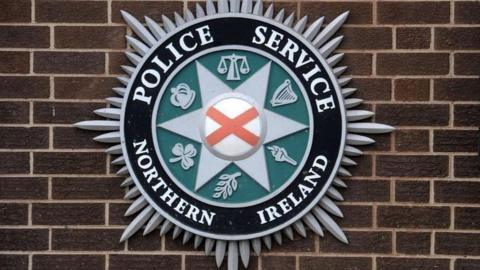 A Police Service of Northern Ireland crest on a brown brick wall 