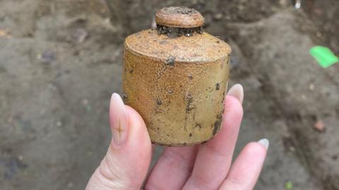 A woman's hand is in the picture holding an ancient pot that was discovered during an archaeological dig.