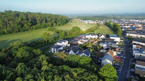 An aerial view of Graven Hill homes and surrounding woods on a sunny day.