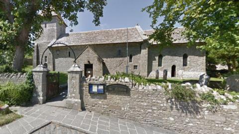 Stone church surrounded by wall with arched entrance.