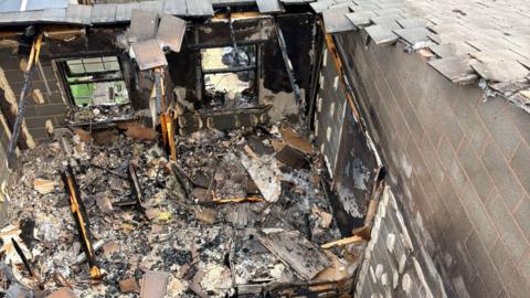Debris left over from a house fire in Derby. There are burnt objects everywhere and charred walls. 