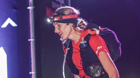 Charlotte Fisher wearing running clothing with a torch on her head running at night