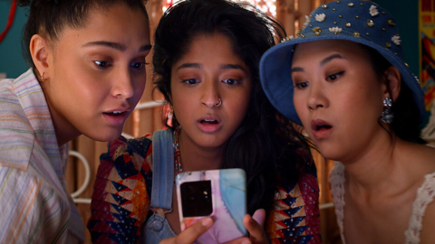 The cast of TV drama Never Have I Ever, three young women, look at a phone with surprise and anticipation 