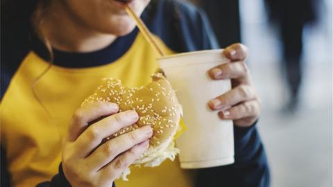 Young girl eating a burger and a fizzy drink