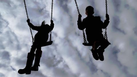 A silhouette shot of a boy and a girl playing on the swings