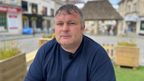  A man in a blue t-shirt siting on a bench in Chippenham town centre