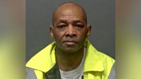 Carson Grimes is clean shaven and wearing a high-vis yellow jacket as he stares at the camera in his police custody photograph