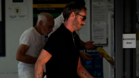 Jack Tweed leaves Chelmsford Magistrates' Court. He is in a black T-shirt and wearing black sunglasses. He has a beard and tattoos of a star on one arm and writing on the other.