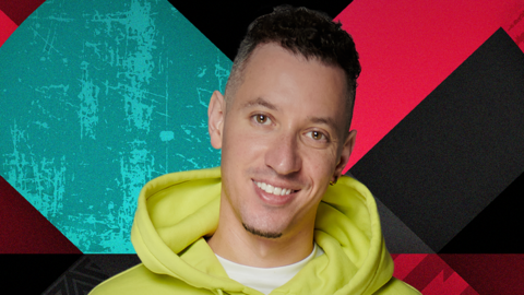 Nick Bright has dark hair and wears a bright yellow hoodie. He is stood in front of a colourful background.