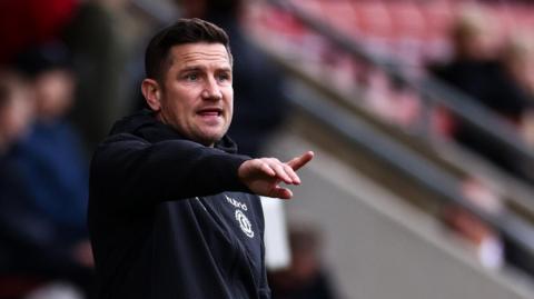 Crewe boss Lee Bell points from the dugout during a match