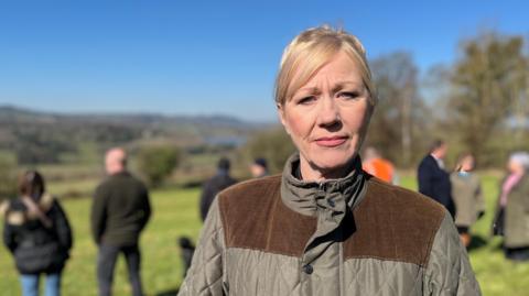 Middle aged woman with blonde hair wearing a padded jacket in a field