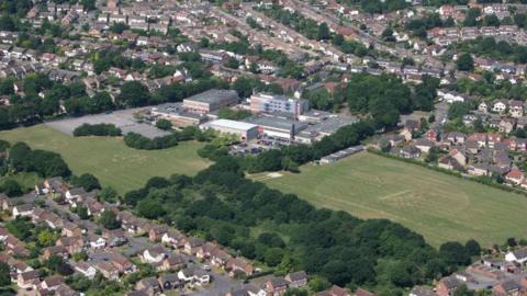 Aerial image of Mayflower High School. The large school building is pictured next to its green school fields. Houses surround the school site.