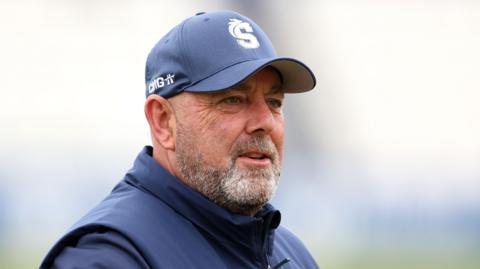 Northamptonshire head coach Darren Lehmann. He is wearing a navy baseball cap with the Northamptonshire Steelbacks logo on the front. 