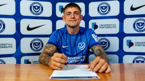 Danish striker Elias Sorensen sat at a desk prepares to sign his three-year contract after agreeing to join Portsmouth FC