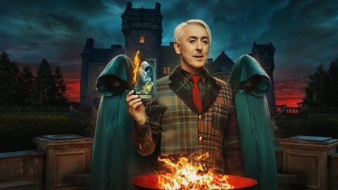 Artwork for The Traitors US featuring Alan Cumming holding a burning card with cloaked people standing behind him. 