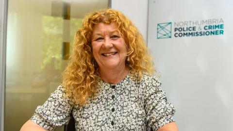 A woman with thick and curly blonde hair smiles at the camera