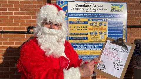 Father Christmas holding a naughty list that says "Excel Parking"