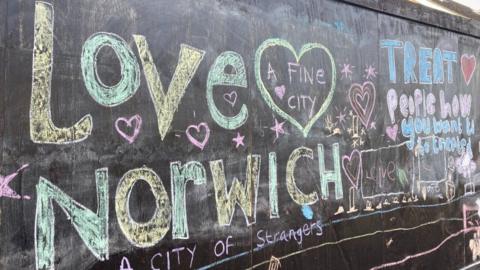A series of chalk messages. The prominent messages in the picture says 'LOVE NORWICH, a fine city, a city of strangers' in yellow and green chalk and 'TREAT PEOPLE HOW YOU WANT TO BE TREATED' in blue and pink writing.