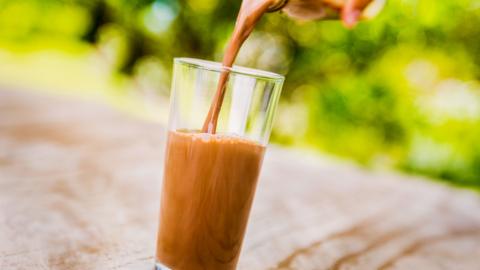 A person pouring chocolate milkshake from bottle into a glass