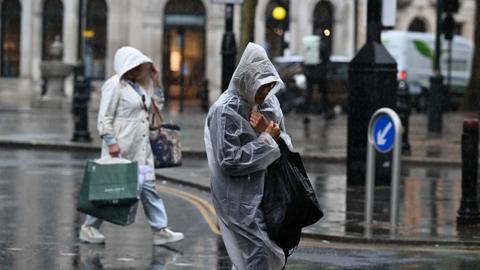 People walking in a street with ponchos and rain jackets, holding their shopping bags cowering from the rain
