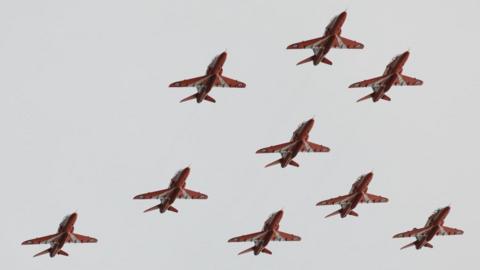 The Red Arrows flying in formation, with a grey sky above them.