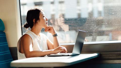 Young business woman looks out the train window while using her laptop on a table