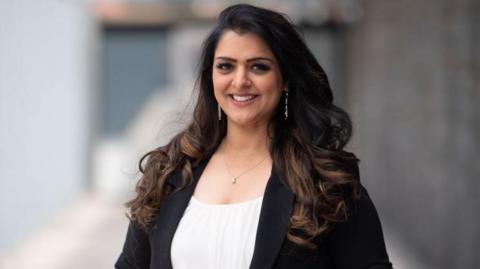 Natasha Asghar standing outside the Senedd in Cardiff Bay, smiling at the camera