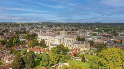 An aerial shot of Winchester Cathedral, surrounded by many red-bricked buildings, trees and grass.