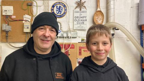 10 year old Alfie Eltham poses in his workshop alongside his grandfather Roy