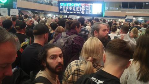 Dense crowd looks at screens at Euston station 