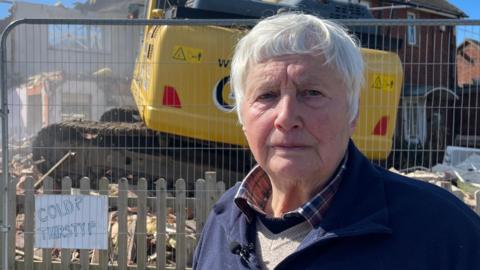 Bryony Nierop-Reading, a woman standing in front of her house which is being demolished. She is looking directly at the camera.