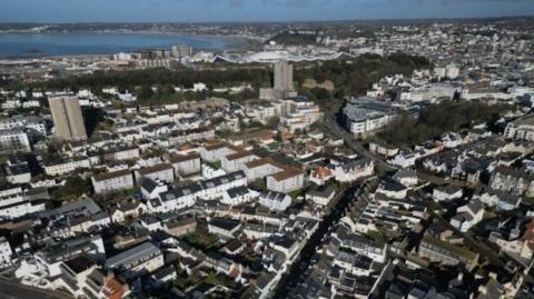 Aerial view of Jersey with high-rise buildings and houses. The sea is the background.