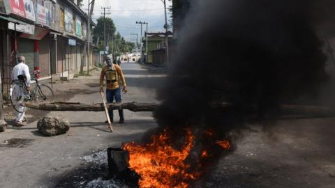 Protesters stand by a burning tyre near a barricade set by them to block the road during a protest against the abolishing of Article 370, on August 20, 2019