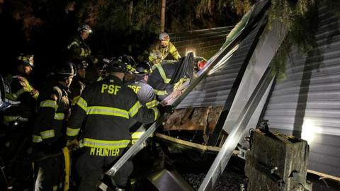 Rescue crews freed two people trapped in a trailer home after a tree fell on them