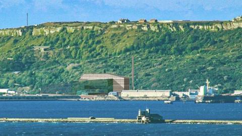 A computer-generated image showing a stone building  built on the seafront, with grassy cliffs rising up behind it