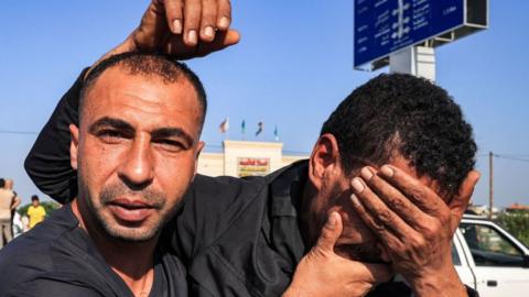 Two Gazan workers near the Kerem Shalom crossing, one holding his face