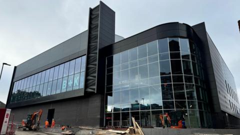 The arena building, with a dark exterior and many glass windows