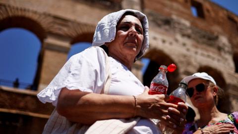 A woman queues near the Colosseum as she shelters from the sun with a towel during a heatwave across Italy