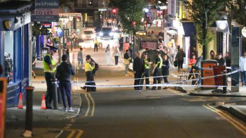 Several police officers stand on the street in a taped off area of St James Street, Brighton